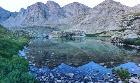 A clear alpine lake surrounded by rocky mountains and green vegetation.