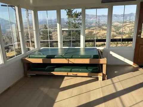 An interior room with large windows overlooking mountains and a wooden bed with green mattresses.