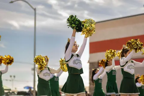 Cheerleaders in green and white uniforms hold up pompoms outdoors.