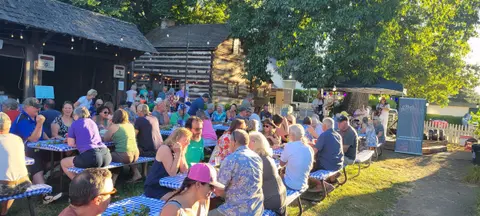 A crowd of people sitting at outdoor picnic tables during an event.