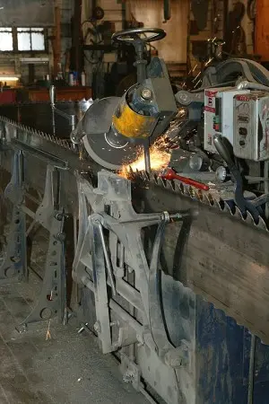 A machine sharpening a large saw blade inside a workshop.