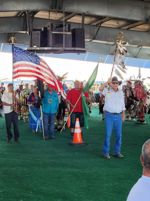 People holding flags and staffs during a gathering under a shelter.