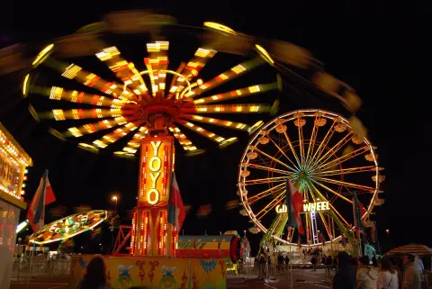 Brightly lit carnival rides spin at night.