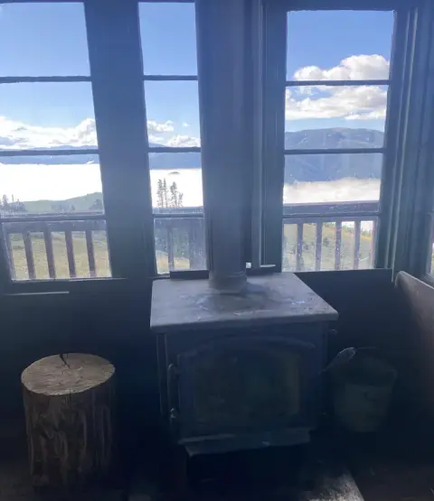 An interior view of a room with a wood-burning stove and large windows overlooking a landscape.
