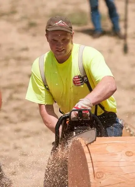 A man uses a chainsaw to cut a log.