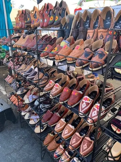A display of many handmade leather sandals and shoes on metal shelves.