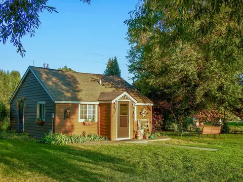 A small cabin stands surrounded by green grass and trees.