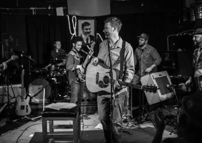 A black and white photo of a band performing on stage indoors.