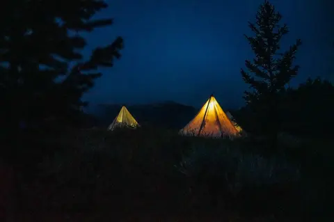 Illuminated tents are set up in a wooded area at night.