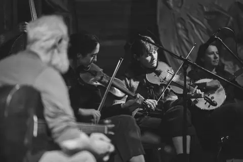 A black and white photograph of musicians playing stringed instruments indoors.