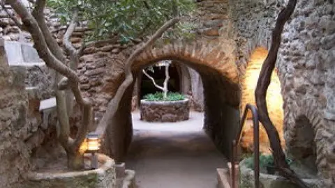 A stone archway and courtyard path with trees and lighting.
