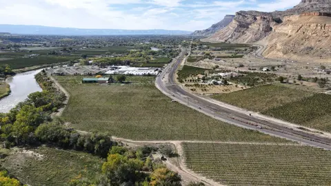 Aerial view of a wide valley with a river, road, railroad, fields, and steep cliffs.