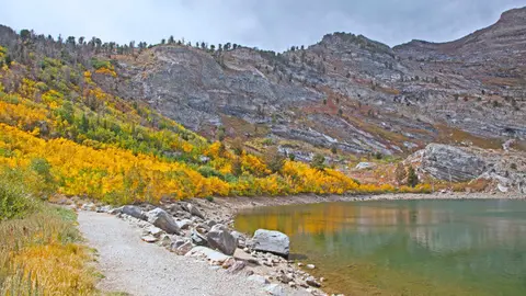 A scenic mountain lake with a walking path and autumn foliage along the shore.