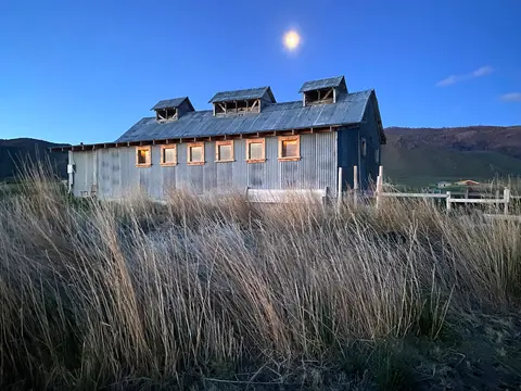 A metal building stands in a field under a blue twilight sky with a bright moon.