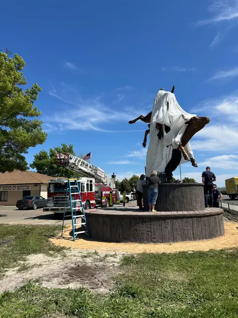 People stand around a covered statue with a fire truck nearby on a sunny day.
