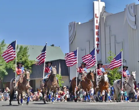 Five equestrians riding horses while carrying American flags during a parade.