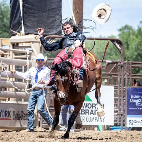A cowboy rides a bucking horse at a rodeo event.