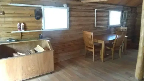 An interior view of a rustic log cabin with a wooden table and chairs.