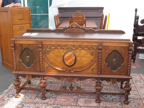 An ornate wooden sideboard stands on a patterned rug outdoors.