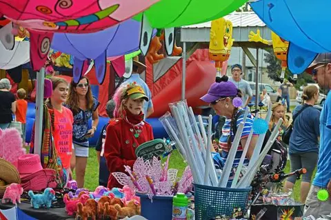 People browse a brightly colored outdoor vendor booth with toys and large hanging inflatables.