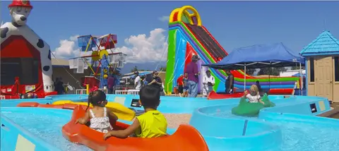 Children ride in small water boats at an outdoor carnival.