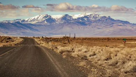 A road leading toward snowy mountains in the distance.