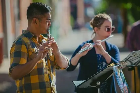 Two people playing flutes outdoors.
