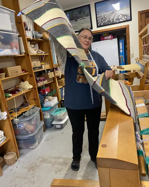 A woman displays a woven textile inside a workshop.
