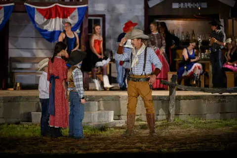 Actors in western costumes perform on an outdoor stage.