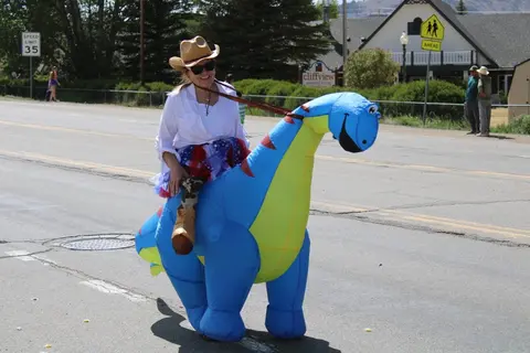 A person rides an inflatable dinosaur costume down a street.
