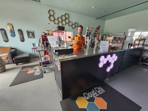 A man stands behind a bar holding up a glass of beverage inside a tasting room.