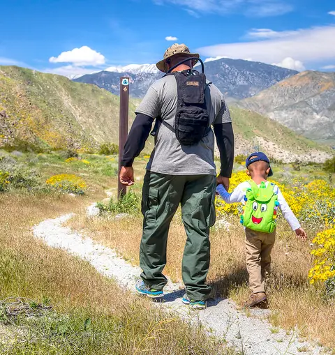 An adult and a child walking on a trail with mountains in the background.