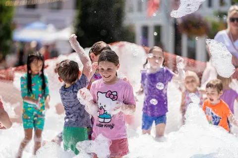 Children play happily in a foam party outdoors.