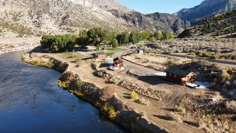 An aerial view of several small cabins situated along a river near mountains.