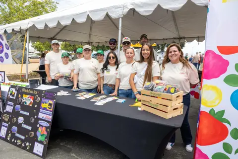A group of people pose behind a booth at an outdoor event.