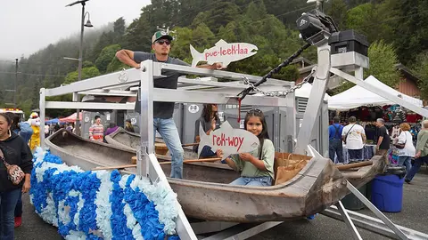 People stand on and around a decorated canoe float with fish-shaped signs during an outdoor event.