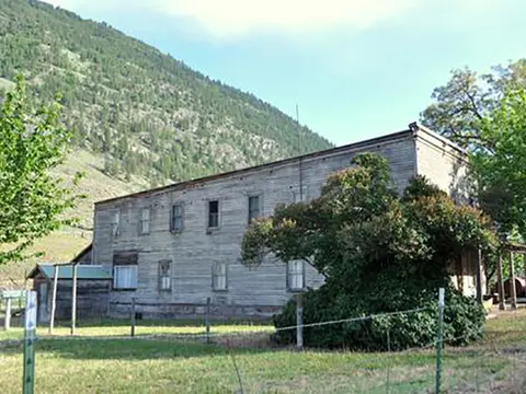 A two-story weathered wooden building sits below a grassy hill.