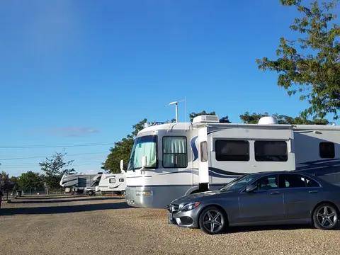 A large recreational vehicle and a car are parked in a gravel lot on a clear day.