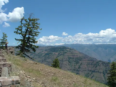 A scenic landscape shows mountains, valleys, and trees under a blue sky with clouds.
