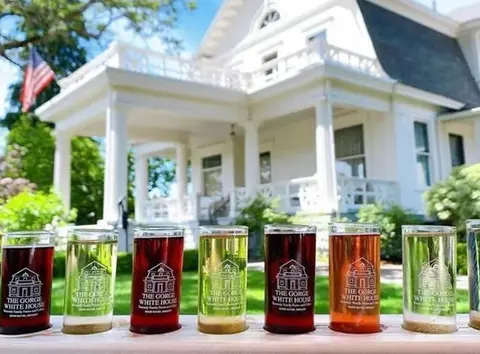 A row of drinks in glasses displayed in front of a large white house.