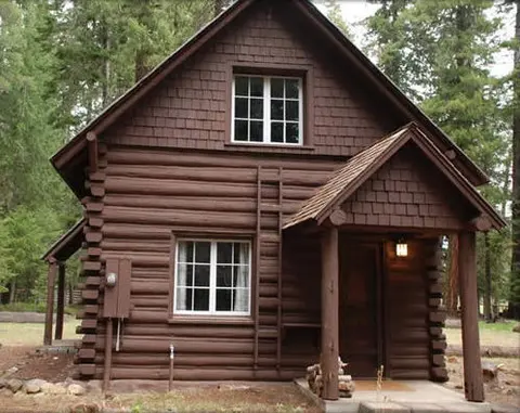 A rustic brown log cabin stands among trees.