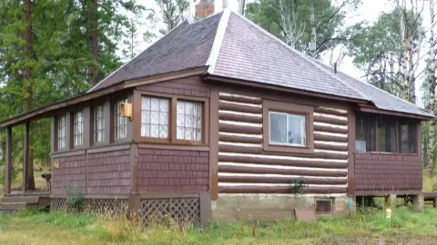 Exterior view of a rustic log cabin surrounded by trees.