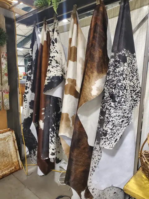 A row of cowhide rugs hangs on display indoors.