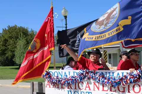 People holding flags on a decorated float in an outdoor event.