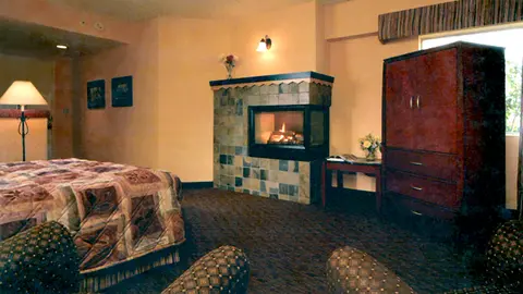 A cozy hotel room interior with a fireplace, bed, and wardrobe.