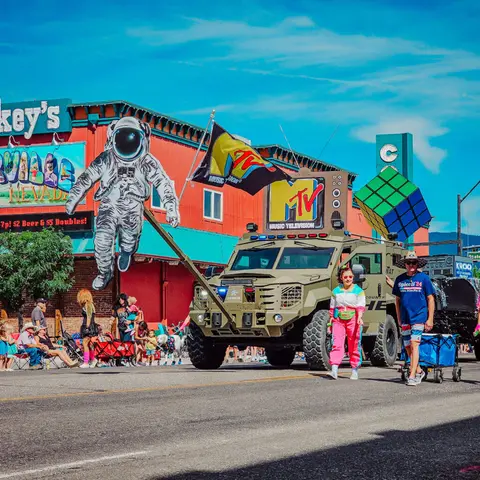 A decorated military-style vehicle with MTV imagery participates in a street parade.
