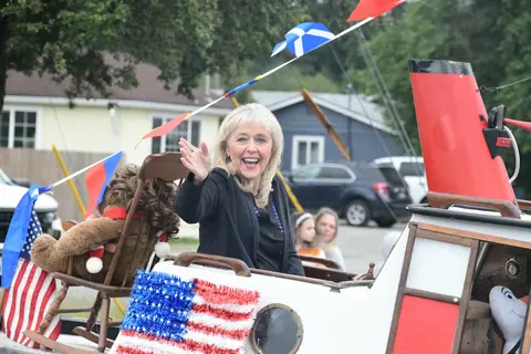 A smiling woman waves from a decorated parade float.