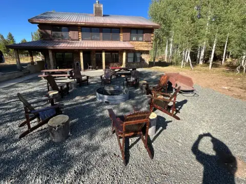 A large log cabin with a gravel courtyard and a fire pit surrounded by wooden chairs.