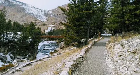 A walking path leads along a mountain river through a forested landscape.