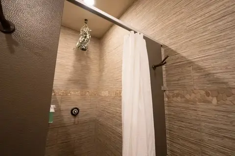 A tiled shower stall with a white curtain.